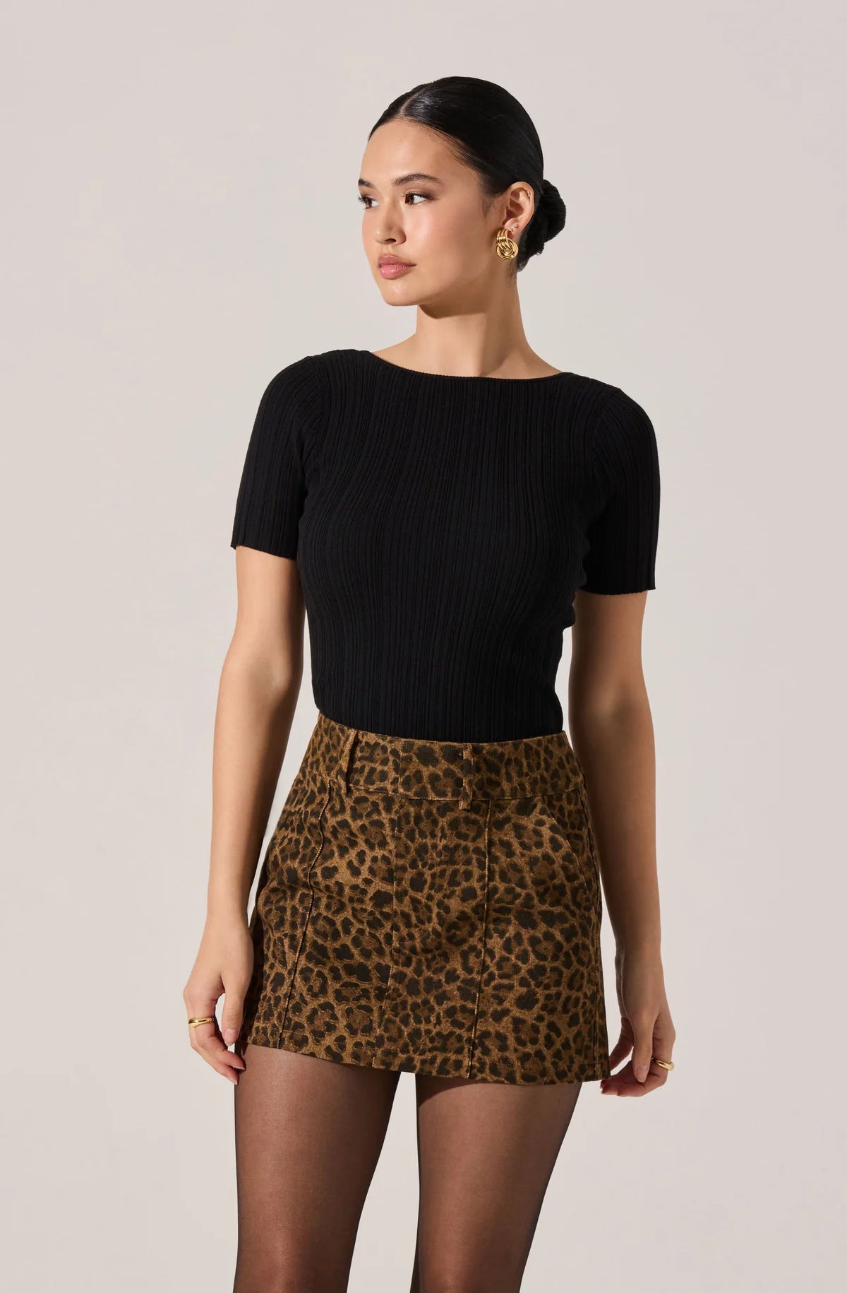 Woman wearing a black top and leopard print skirt on a plain background