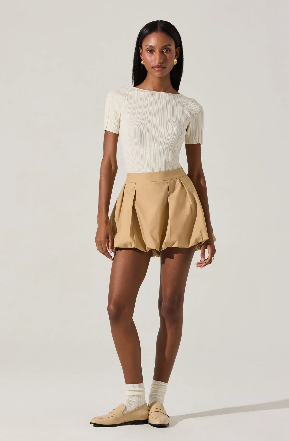 Woman wearing a white top and beige skirt on a plain background