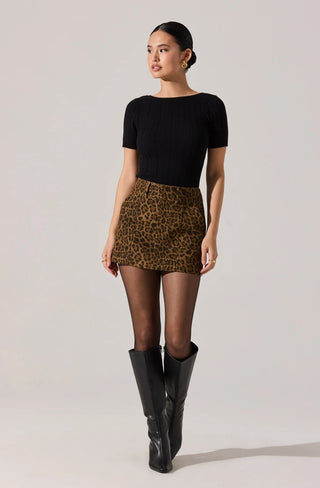 Woman wearing a black top, leopard print skirt, and black rain boots on a plain background