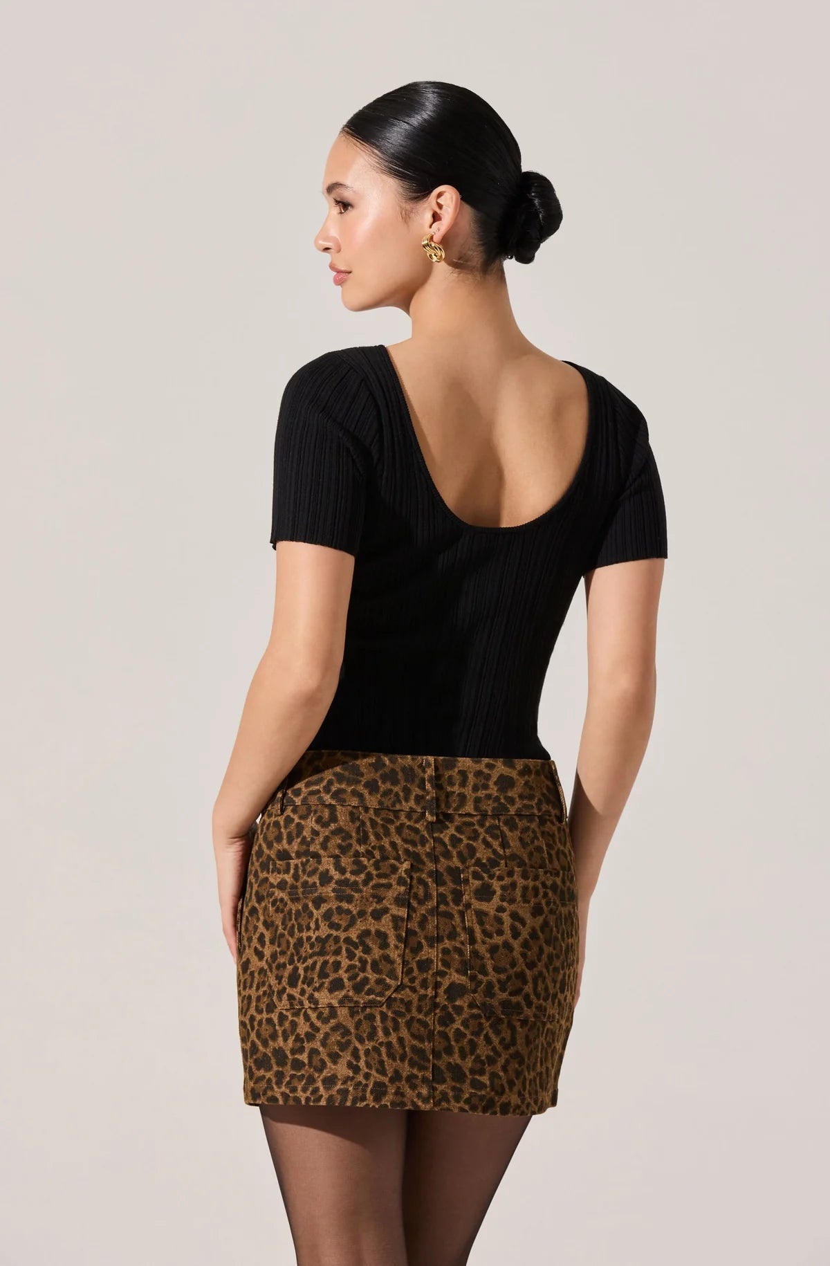 Woman wearing a black top and leopard print skirt against a plain background