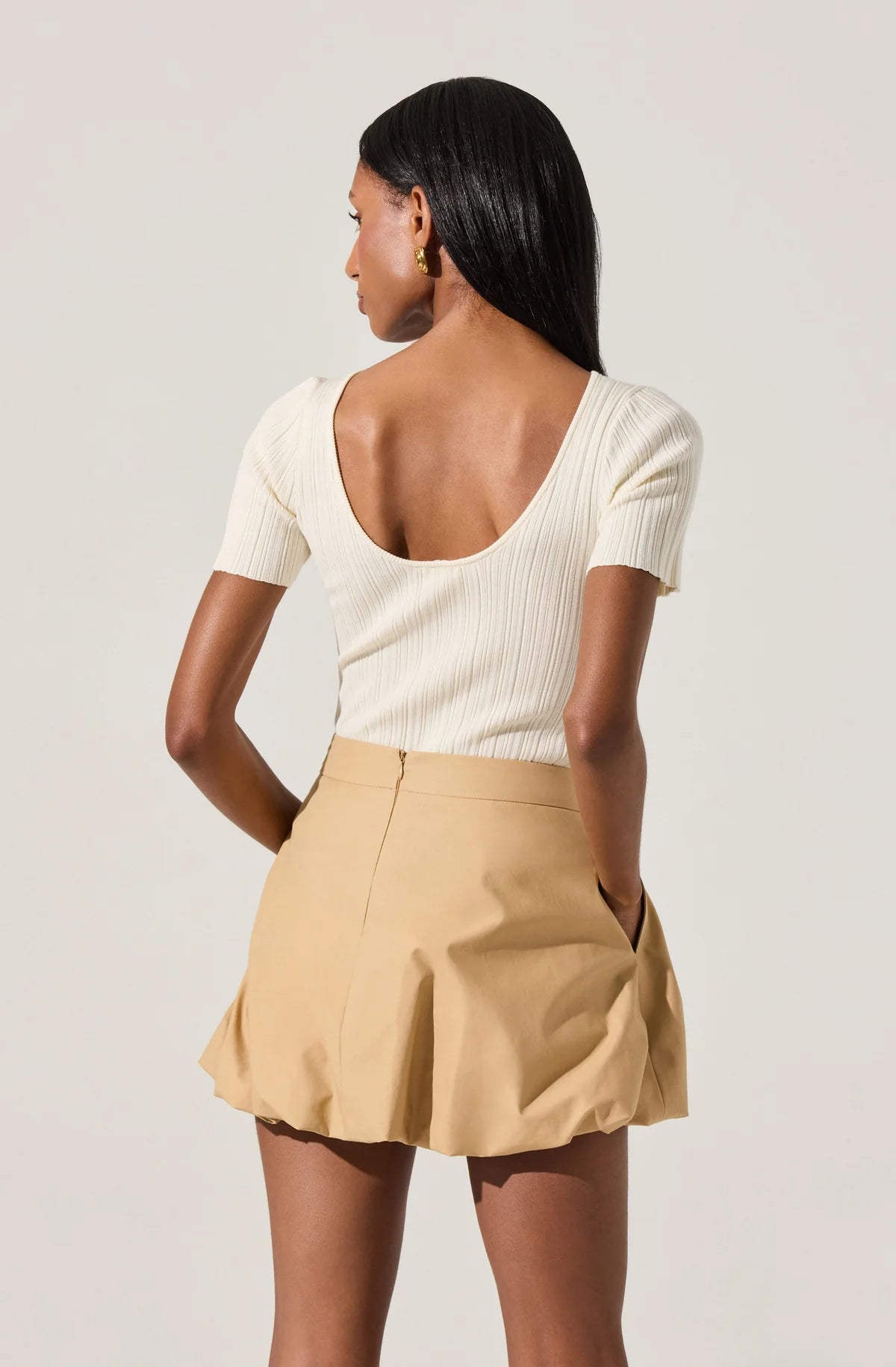 Woman wearing a white ribbed top and beige shorts against a plain background