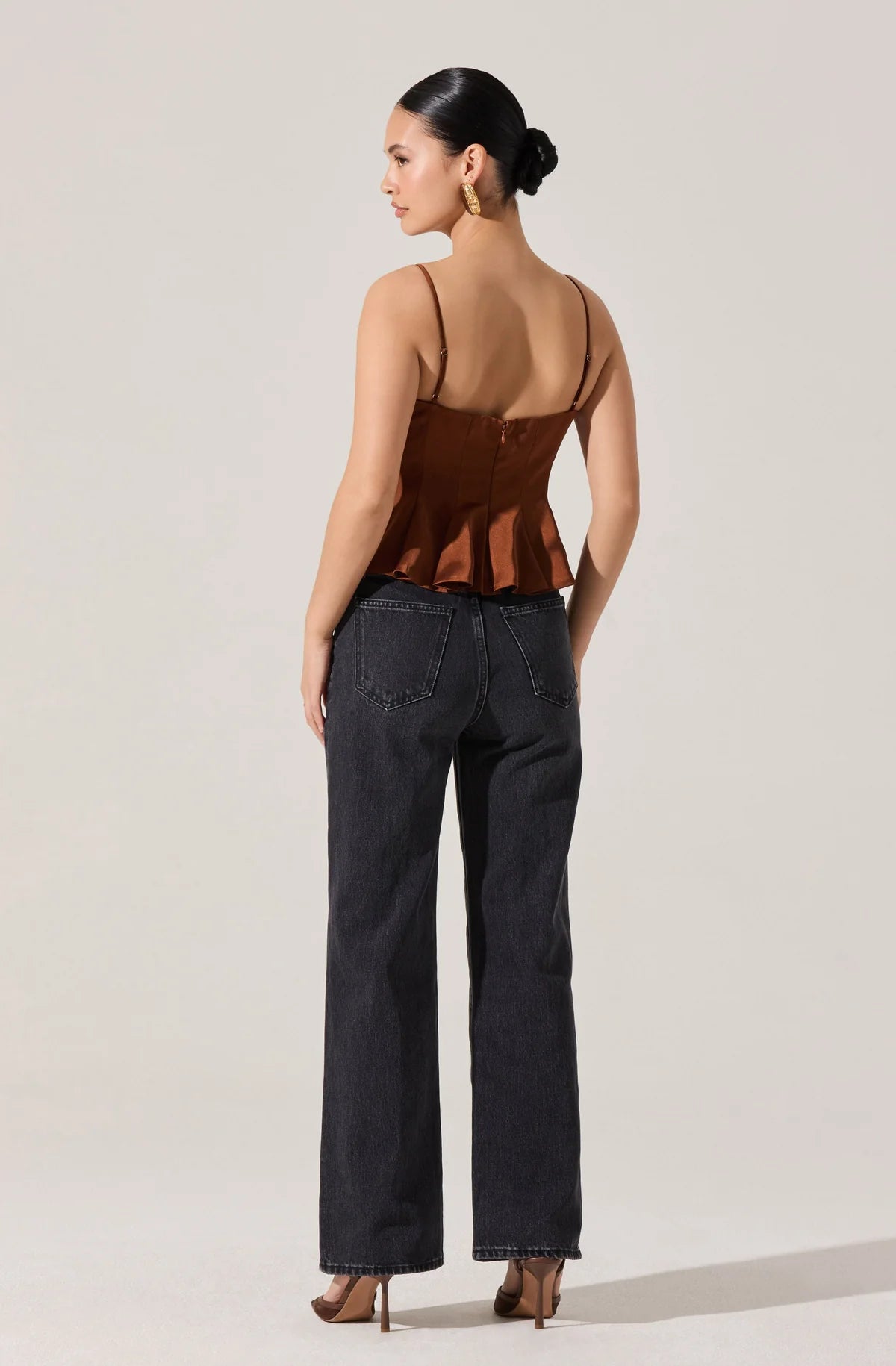 Woman wearing a brown open-back top and black jeans on a light gray background
