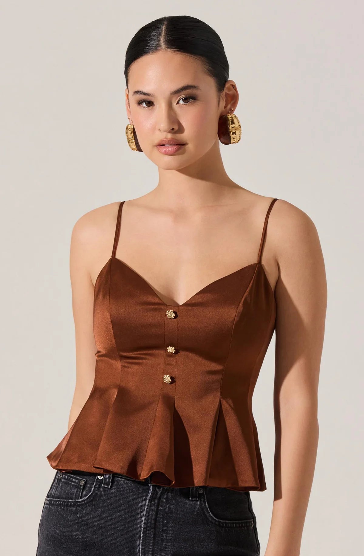 Woman wearing a brown satin top with thin straps against a plain background
