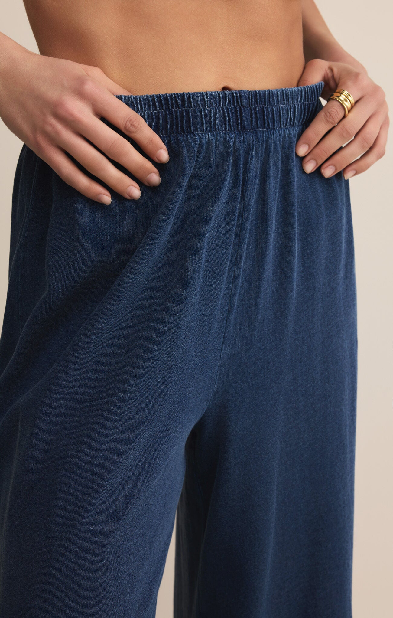 Navy blue pants being adjusted by a person on a beige background