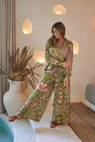 A model wearing wide-leg green pants with a nature-inspired pattern, including images of leaves and butterflies.