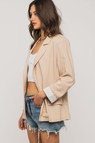 Woman wearing a beige blazer over a white top and denim shorts on a plain background