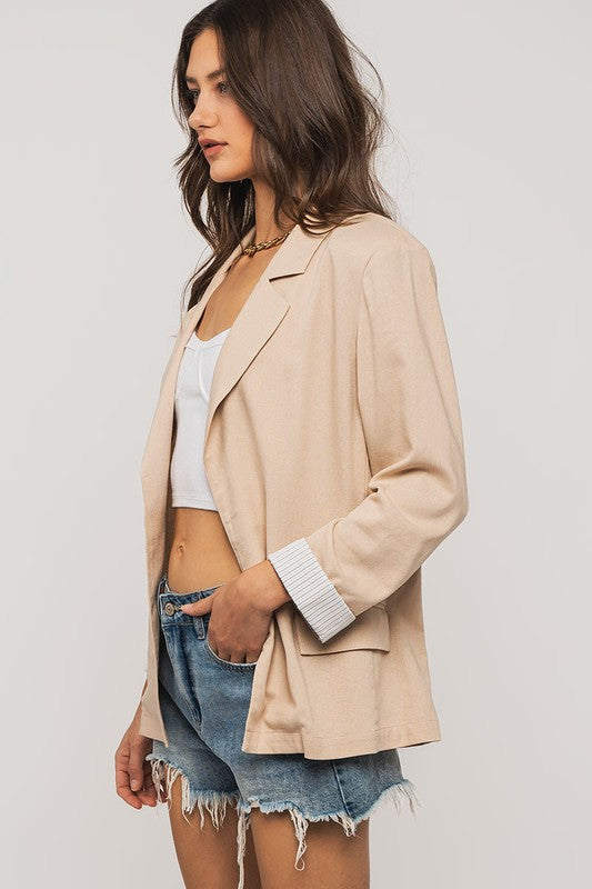 Woman wearing a beige blazer, white top, and denim shorts on a plain background