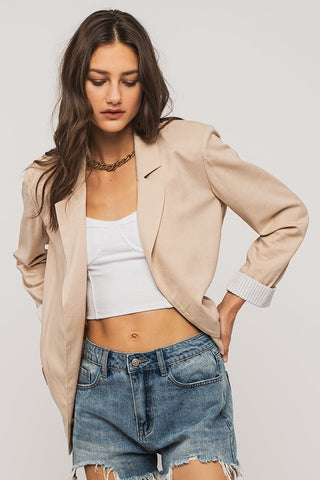 Woman wearing a beige blazer, white top, and denim shorts on a plain background