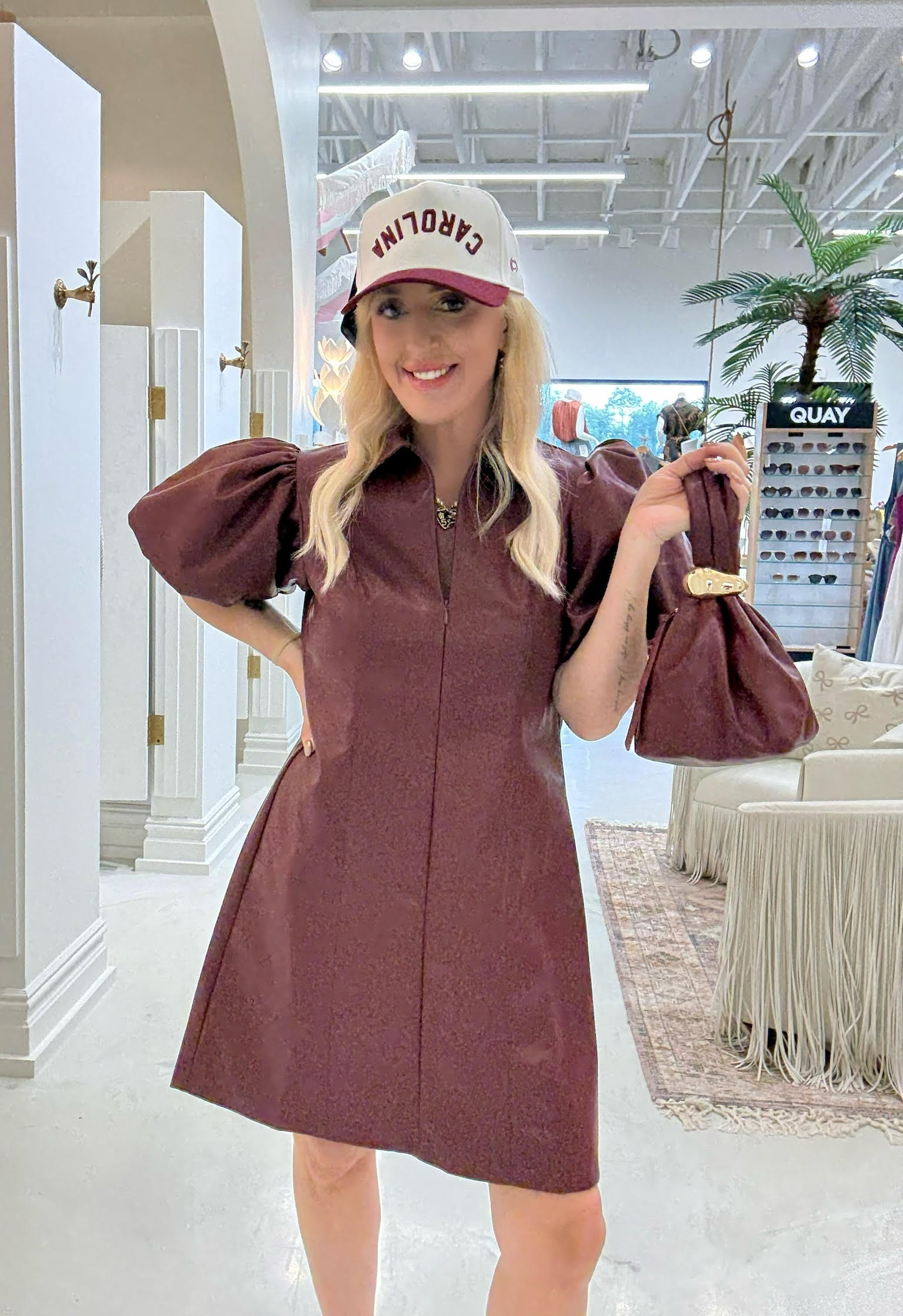 Woman in a maroon dress and cap holding a bag in a store setting
