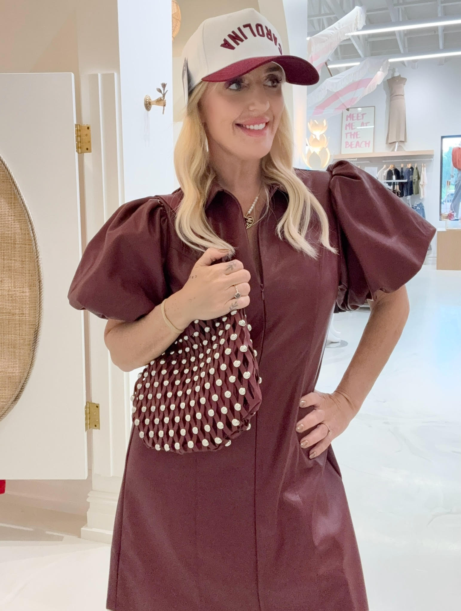 Woman wearing a maroon dress with puff sleeves and a matching polka dot bag indoors.