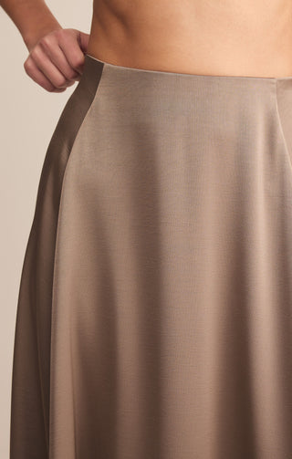 Close-up of a person wearing a beige satin skirt against a neutral background