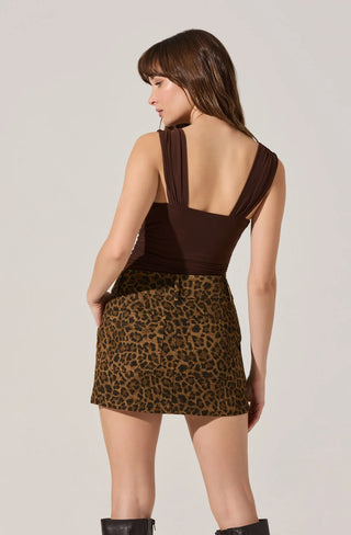 Woman wearing a brown halter top and leopard print skirt on a plain background