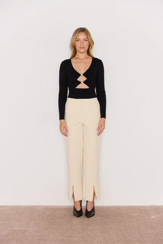 Woman wearing a black top with cut-out design and beige pants on a white background