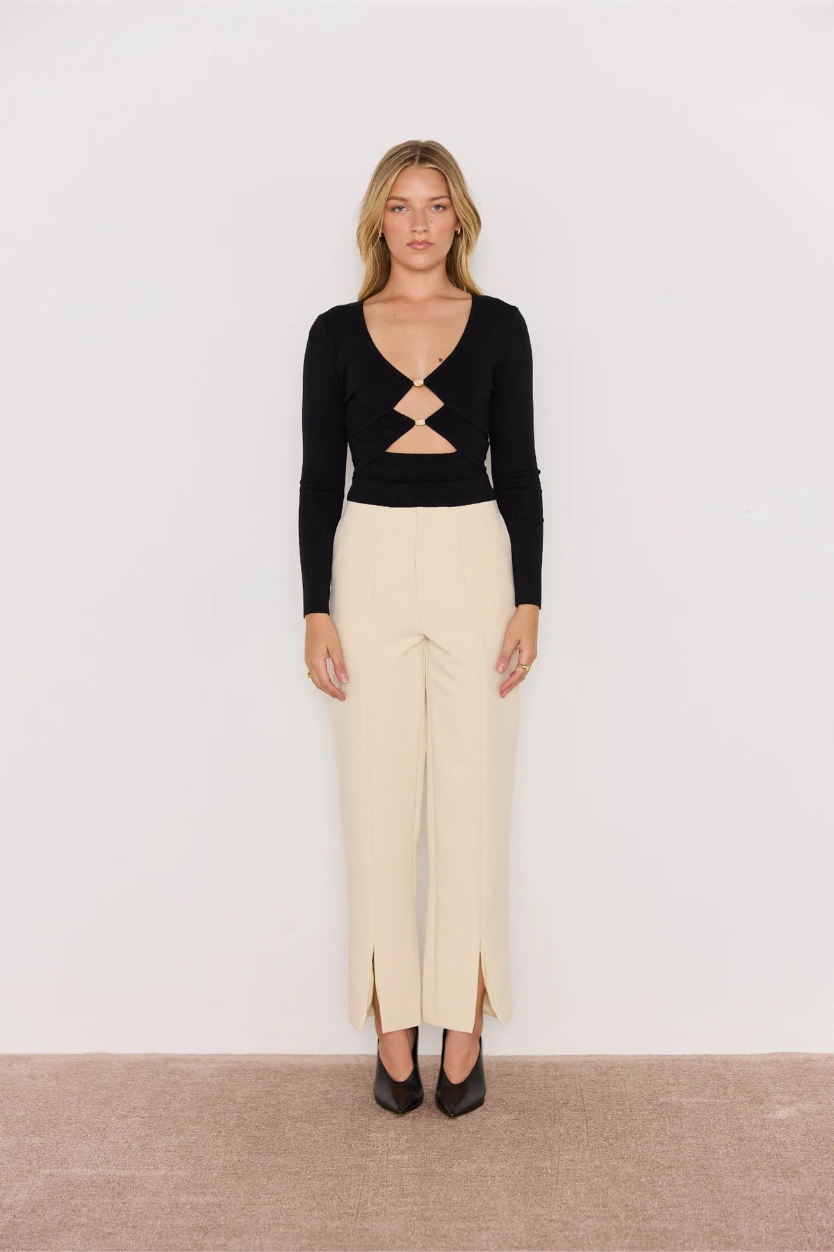 Woman wearing a black top with cut-out design and beige pants on a white background