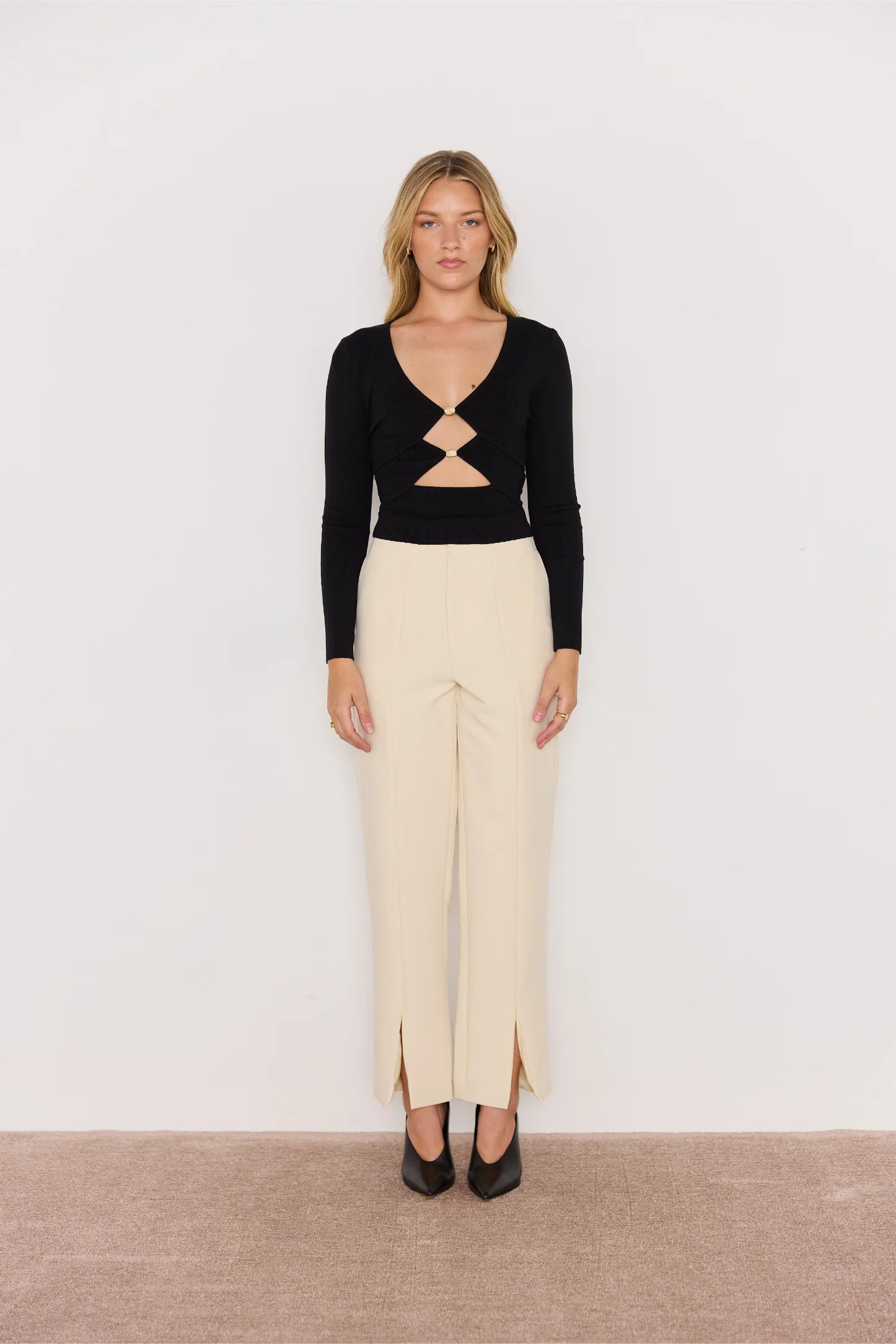 Woman wearing a black long-sleeve top with cut-out design and beige pants on a white background