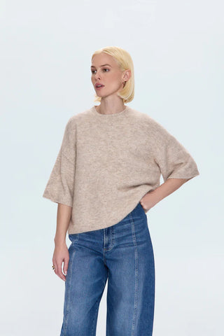 Woman wearing a beige sweater and blue jeans on a light gray background
