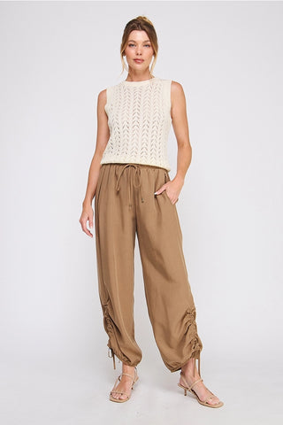 Woman wearing a white sleeveless top and brown high-waisted pants on a white background