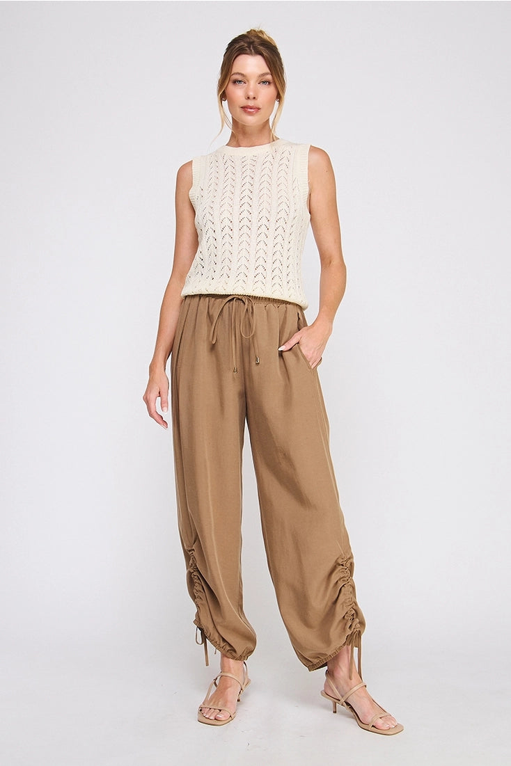 Woman wearing a white sleeveless top and brown high-waisted pants on a white background