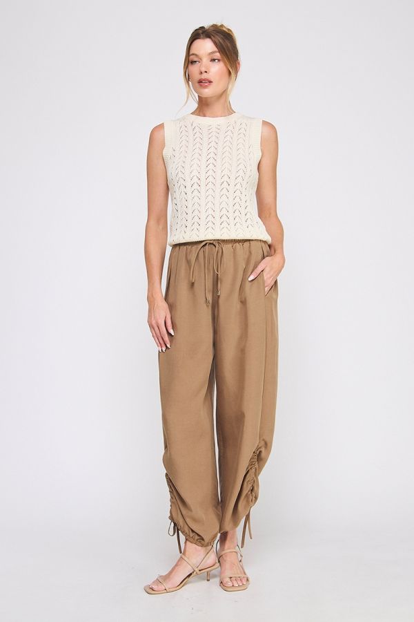 Woman wearing a white sleeveless top and tan pants on a white background
