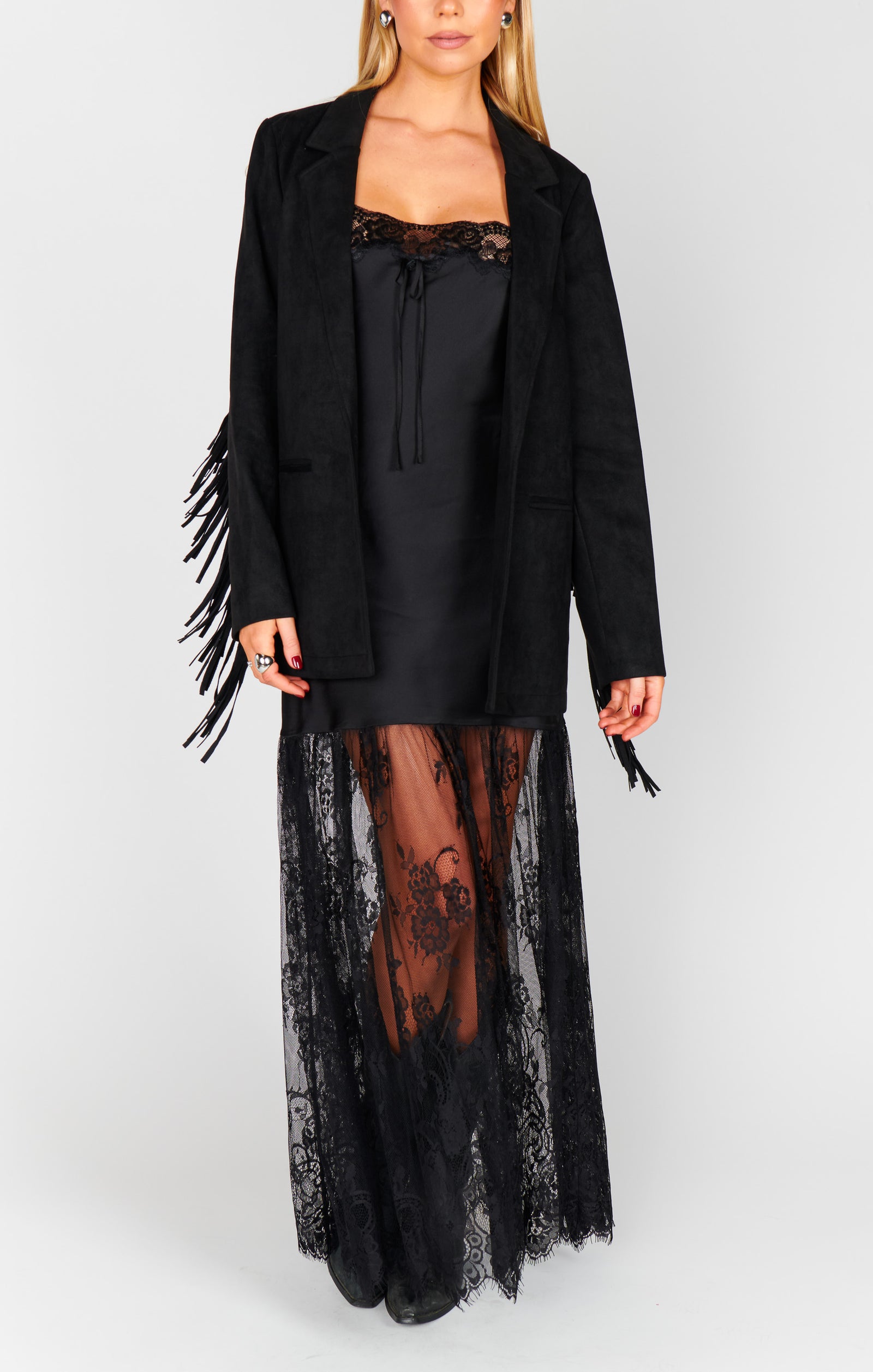 Person wearing a black fringe jacket and lace dress on a plain background