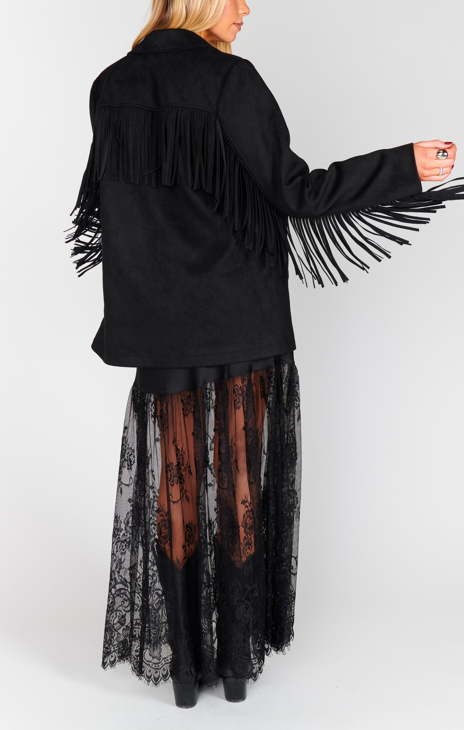 A model wearing a black fringe jacket with long sleeves and a maxi black lace skirt.