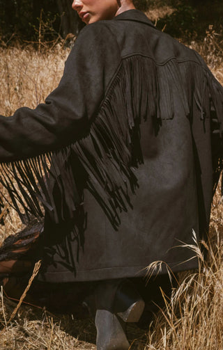 Person wearing a black fringed jacket in a natural setting