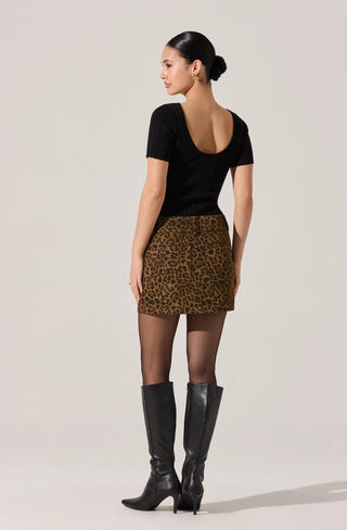 Woman wearing a black top and leopard print skirt with black boots on a plain background