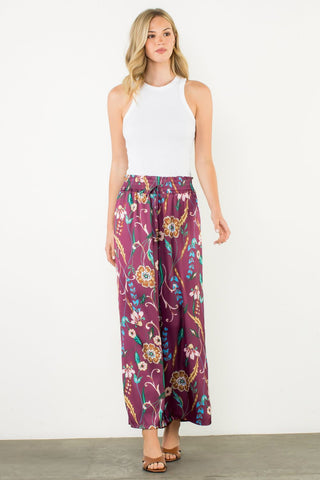 Woman wearing a white sleeveless top and purple floral pants on a white background