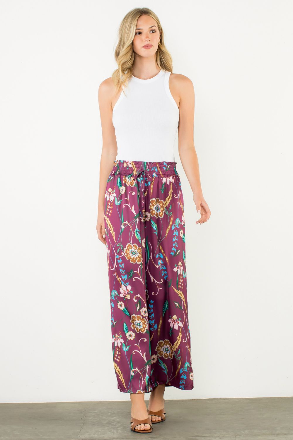 Woman wearing a white sleeveless top and purple floral pants on a white background