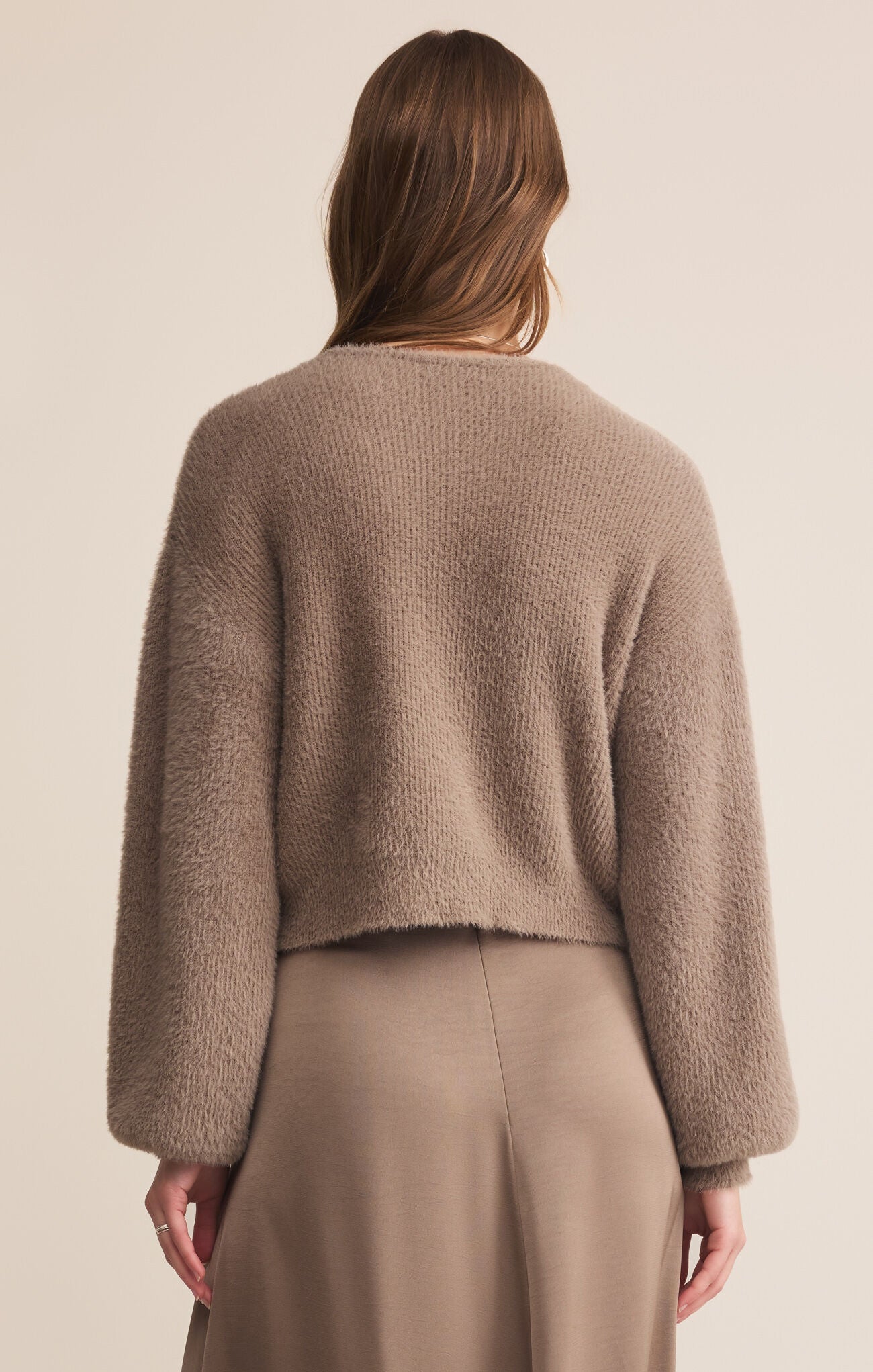 Person wearing a brown sweater and beige pants against a plain background