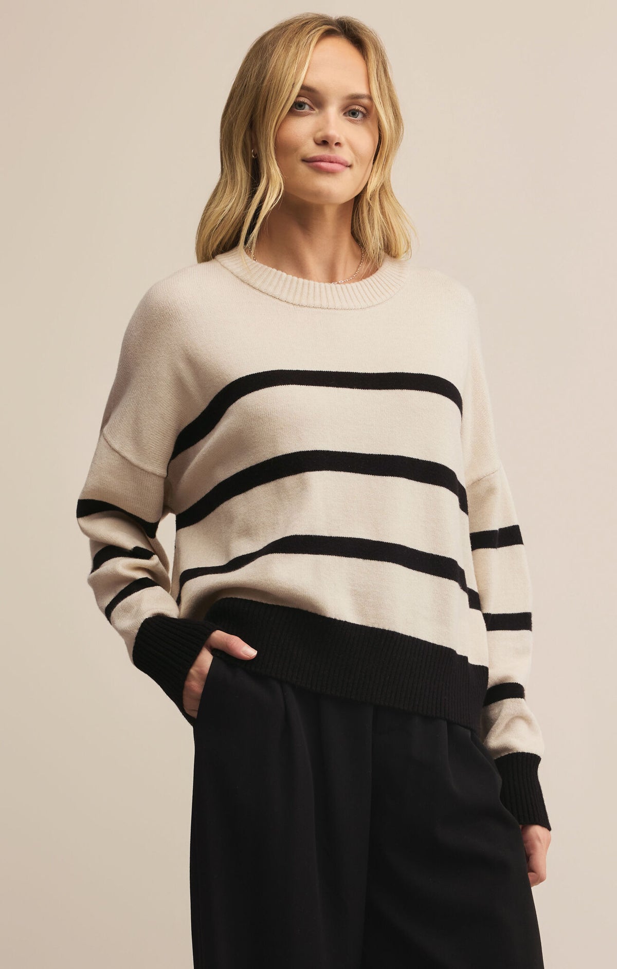 Woman wearing a cream sweater with black stripes and black pants on a beige background
