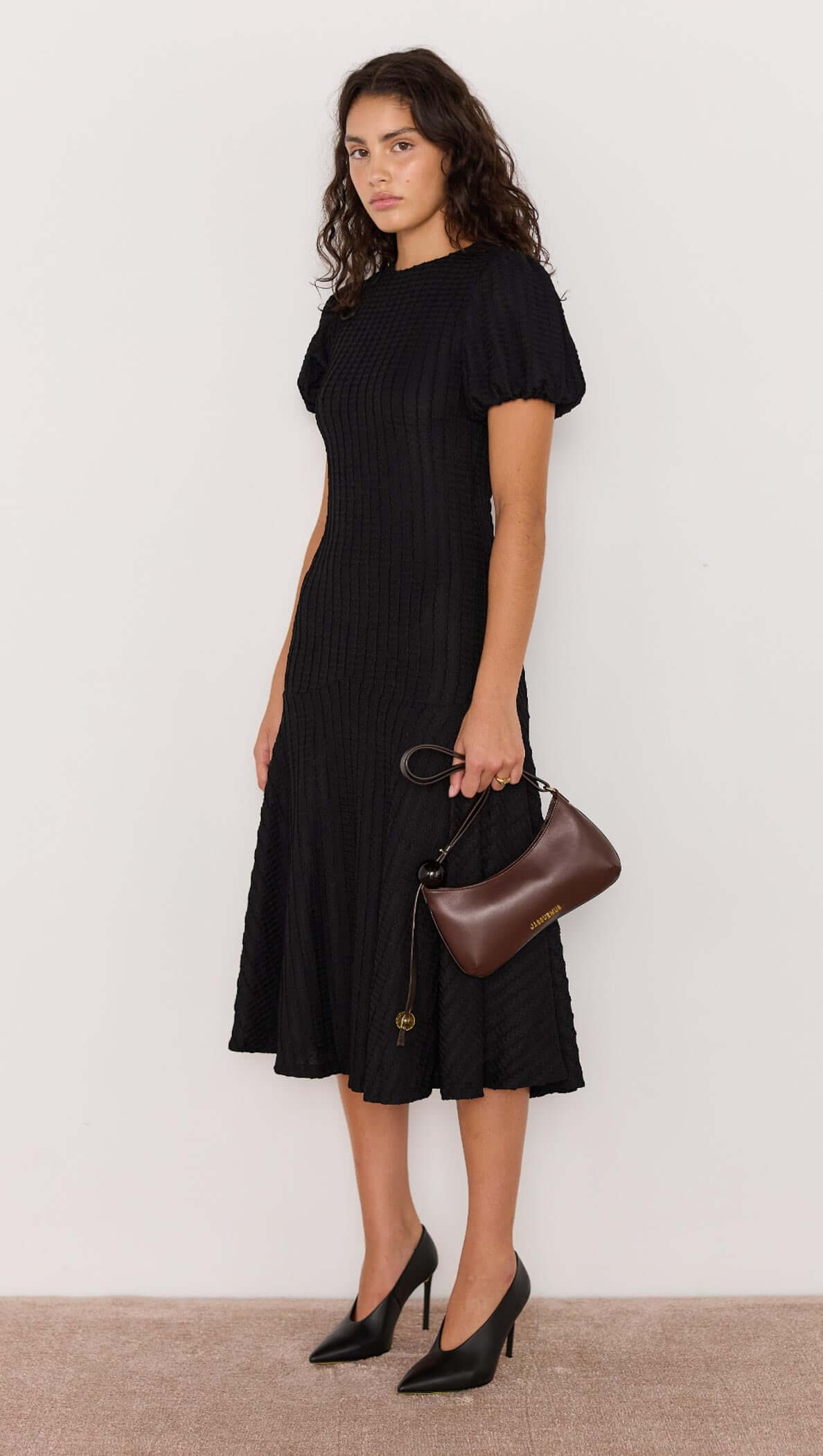 Woman wearing a black dress holding a brown handbag against a white background