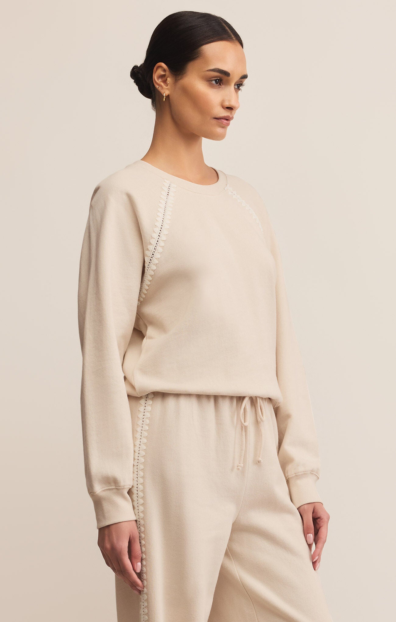 Woman wearing a beige sweatshirt and pants on a plain background