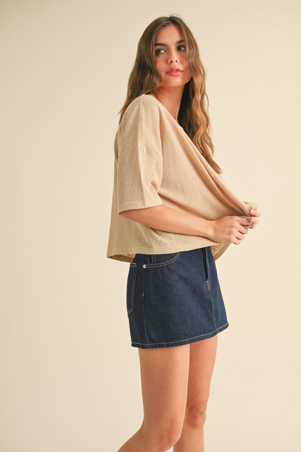 Woman wearing a beige top and denim skirt on a beige background