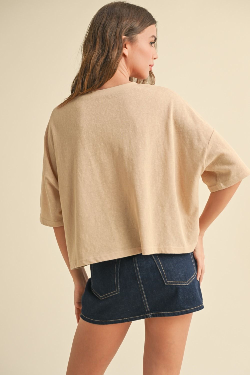 Woman wearing a beige oversized shirt and denim skirt on a beige background