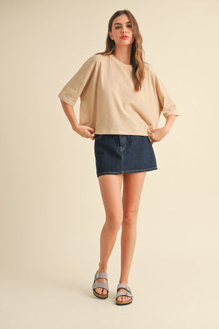 Woman wearing a beige top and denim skirt on a beige background