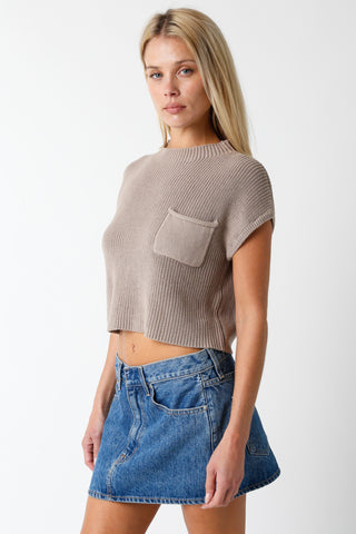 Woman wearing a beige ribbed crop top and blue denim skirt on a white background