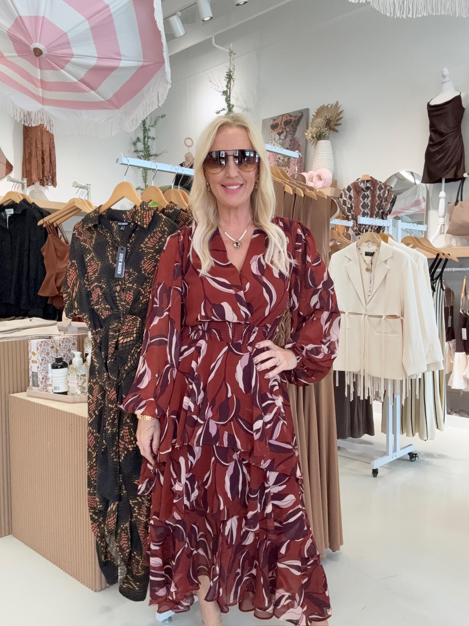 Woman in a patterned dress standing in a clothing store with racks of clothes in the background.