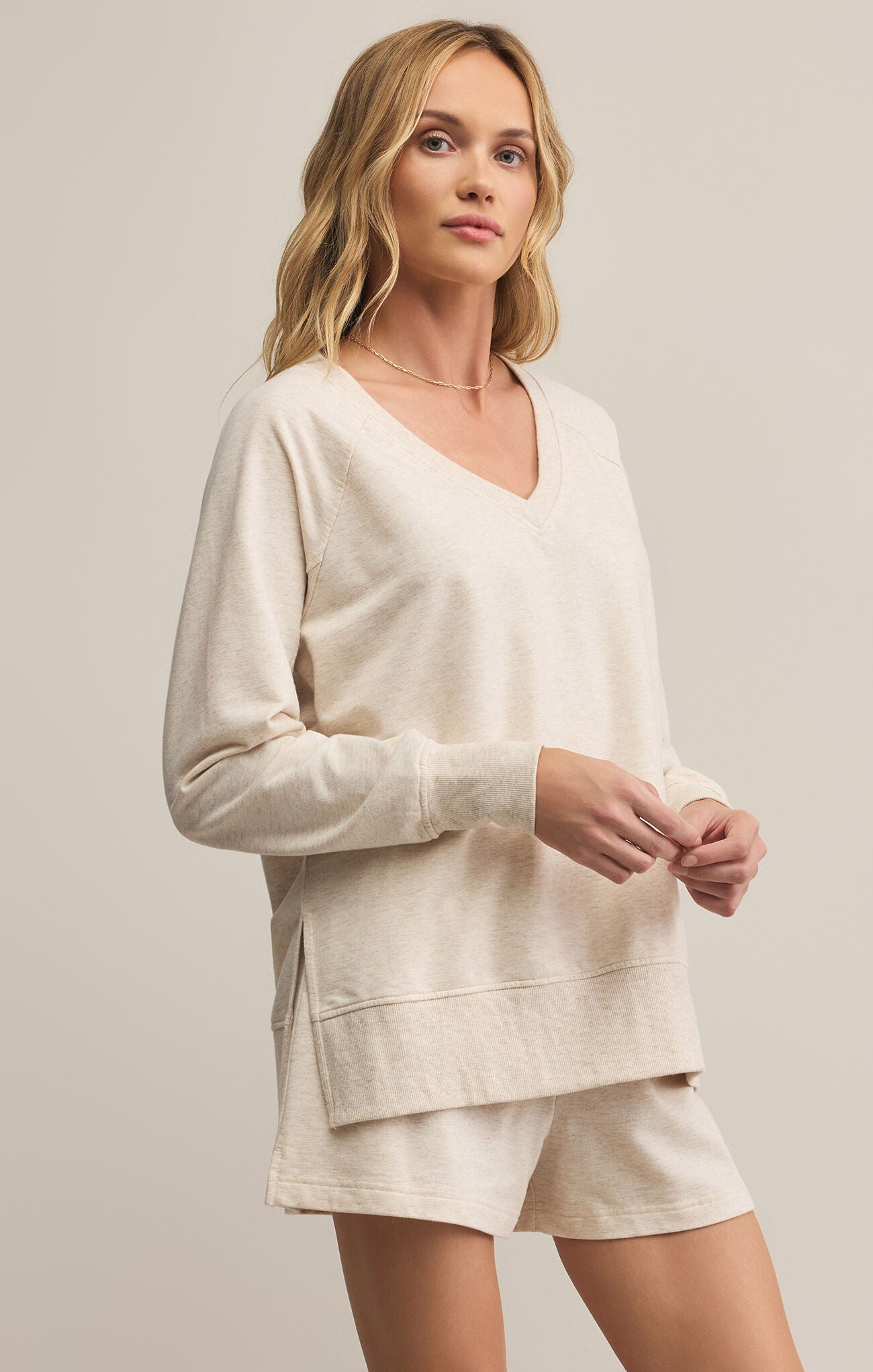 Woman wearing a beige long-sleeve top and shorts on a plain background