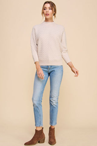 Woman wearing a beige sweater, light blue jeans, and brown boots on a beige background