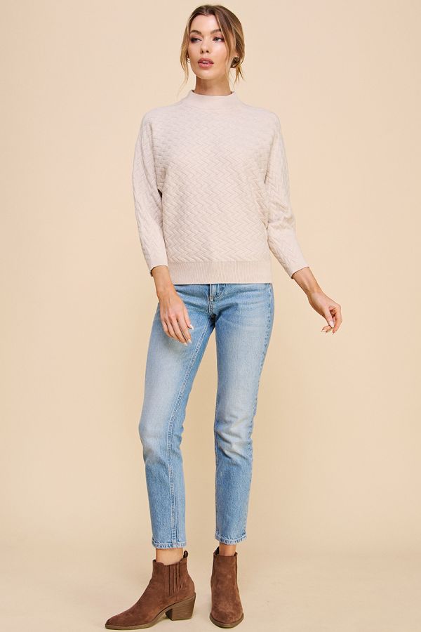 Woman wearing a beige sweater, light blue jeans, and brown boots on a beige background