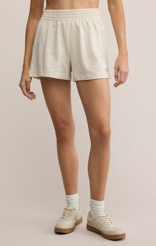 Person wearing cream shorts and white sneakers on a plain background