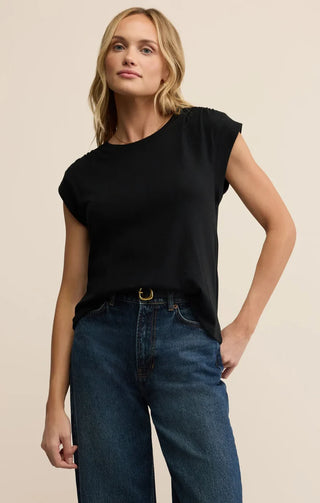 Woman wearing a black sleeveless top and blue jeans against a beige background
