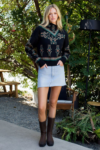 Woman wearing a dark sweater with a pattern, light blue denim skirt, and brown boots outdoors.