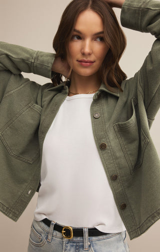 Woman wearing a green jacket over a white shirt with a beige background