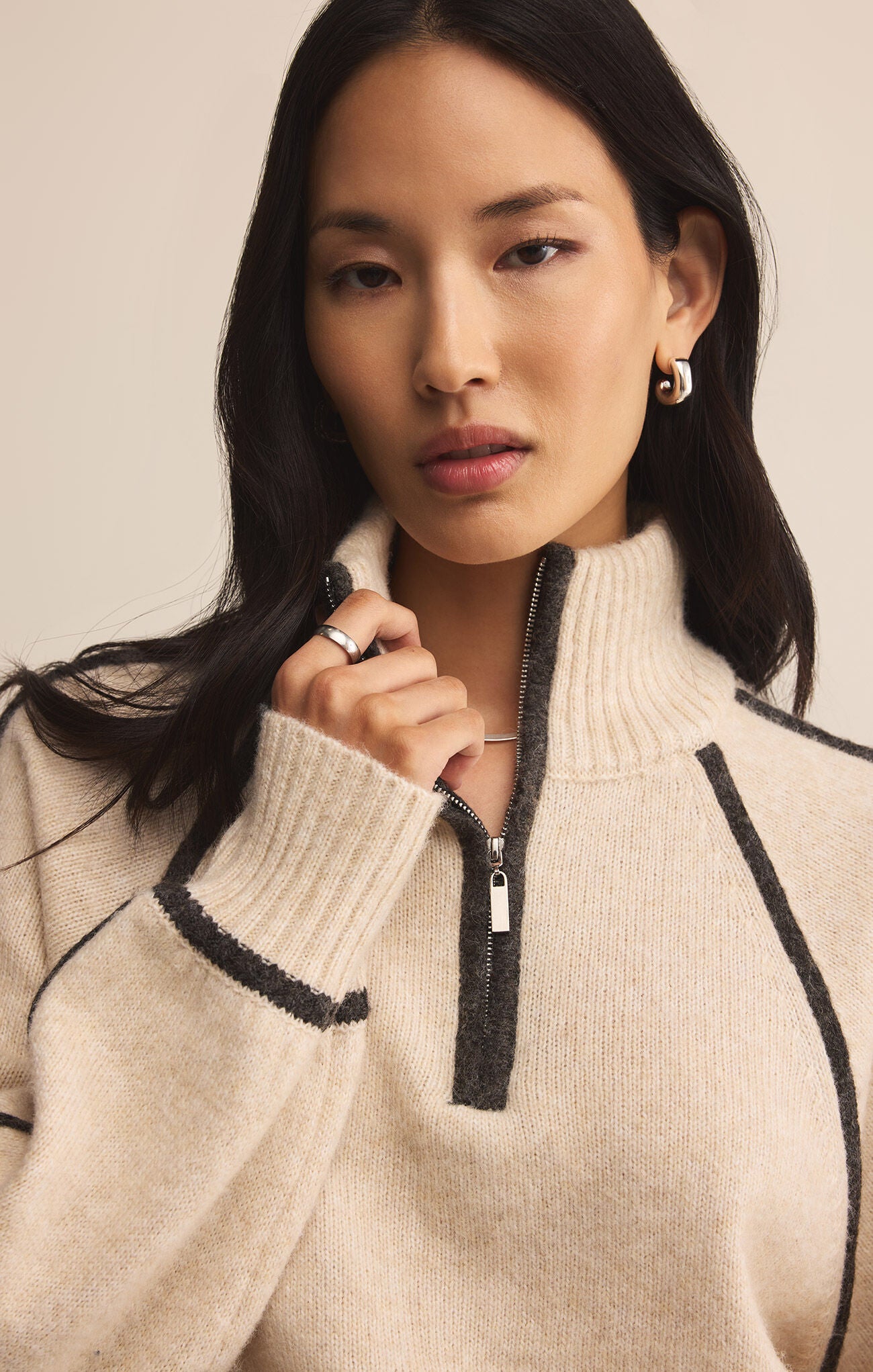 Woman wearing a beige sweater with black accents on a neutral background