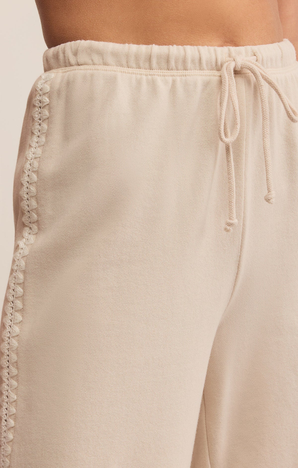 Beige pants with lace trim and drawstring on a light background