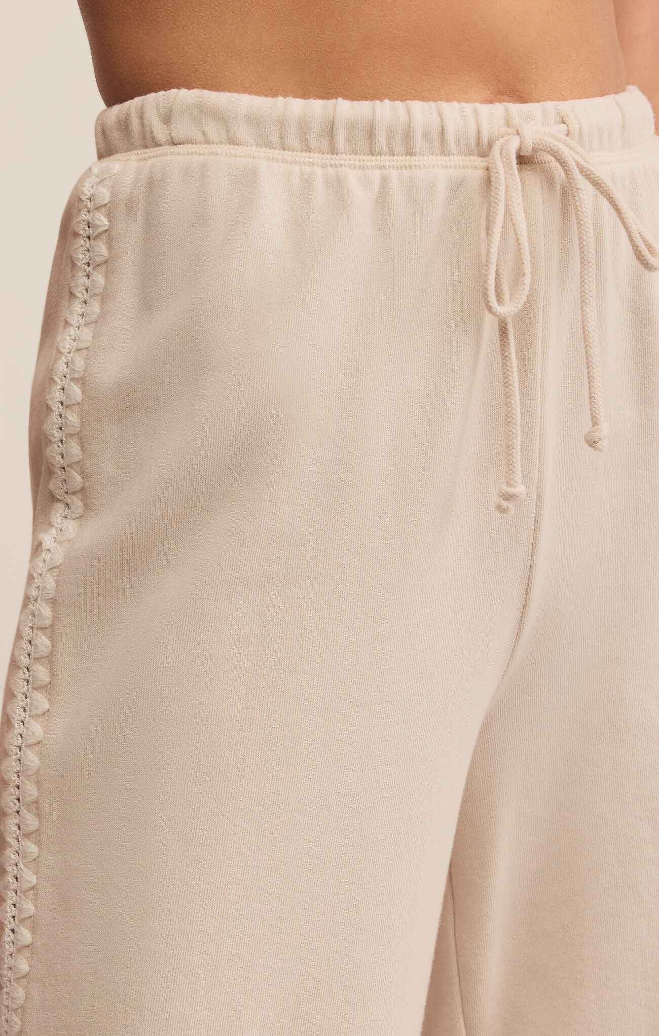 Beige pants with lace trim and drawstring on a light background
