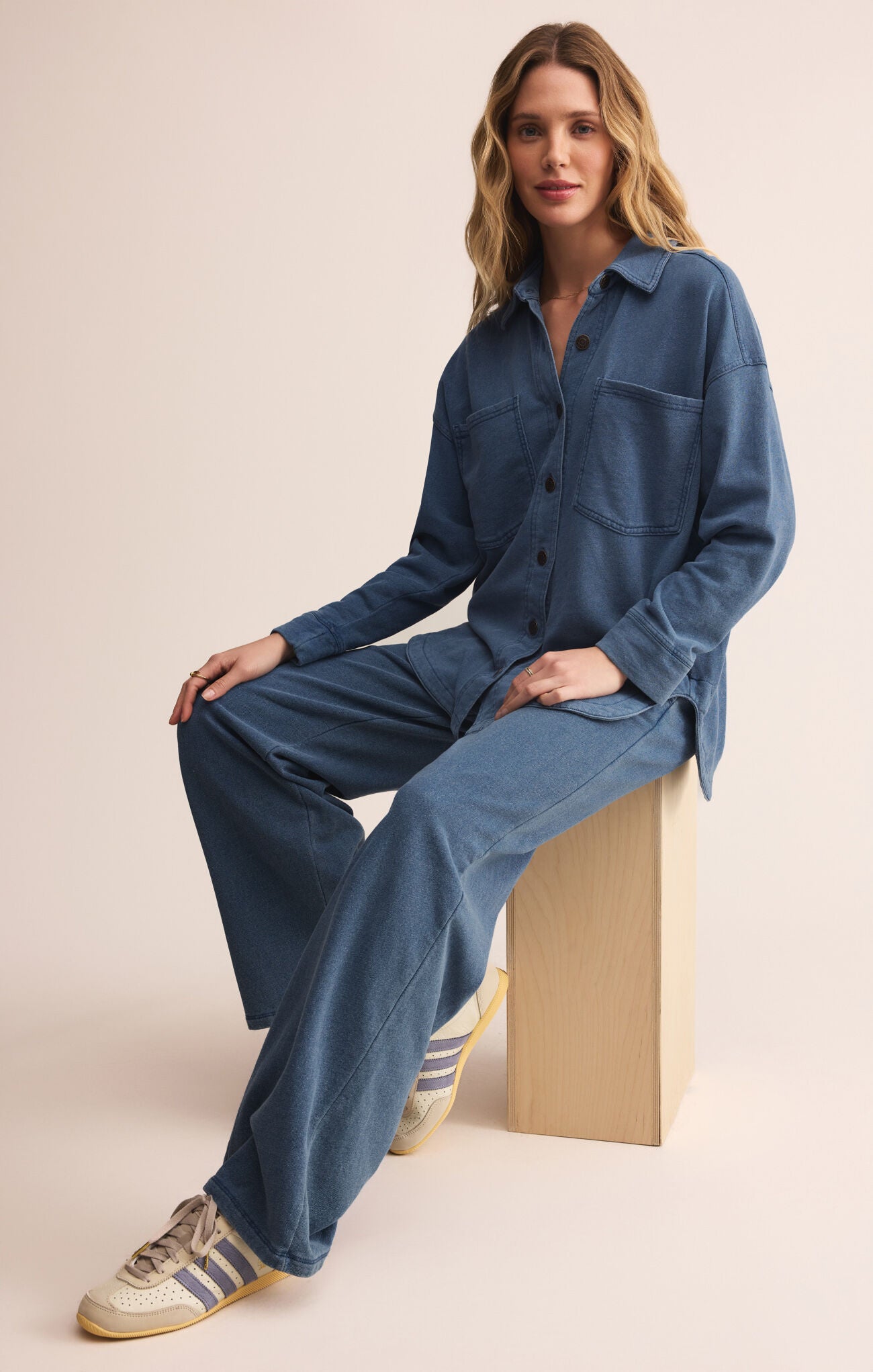 Woman wearing a blue outfit sitting on a wooden block against a beige background