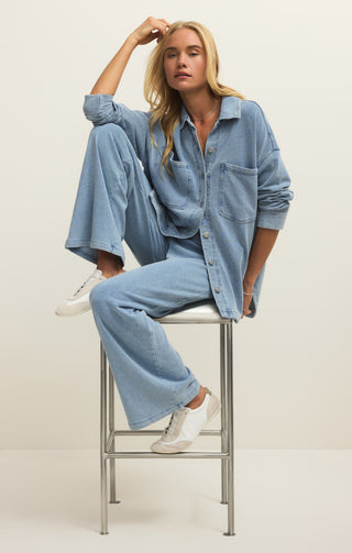 Woman wearing a denim outfit sitting on a stool against a plain background